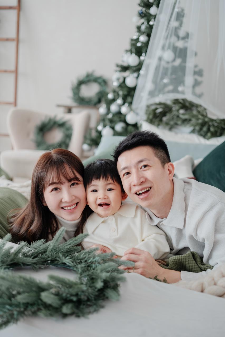 一家三口在聖誕樹旁的座椅上相聚,小朋友坐在大人懷裏