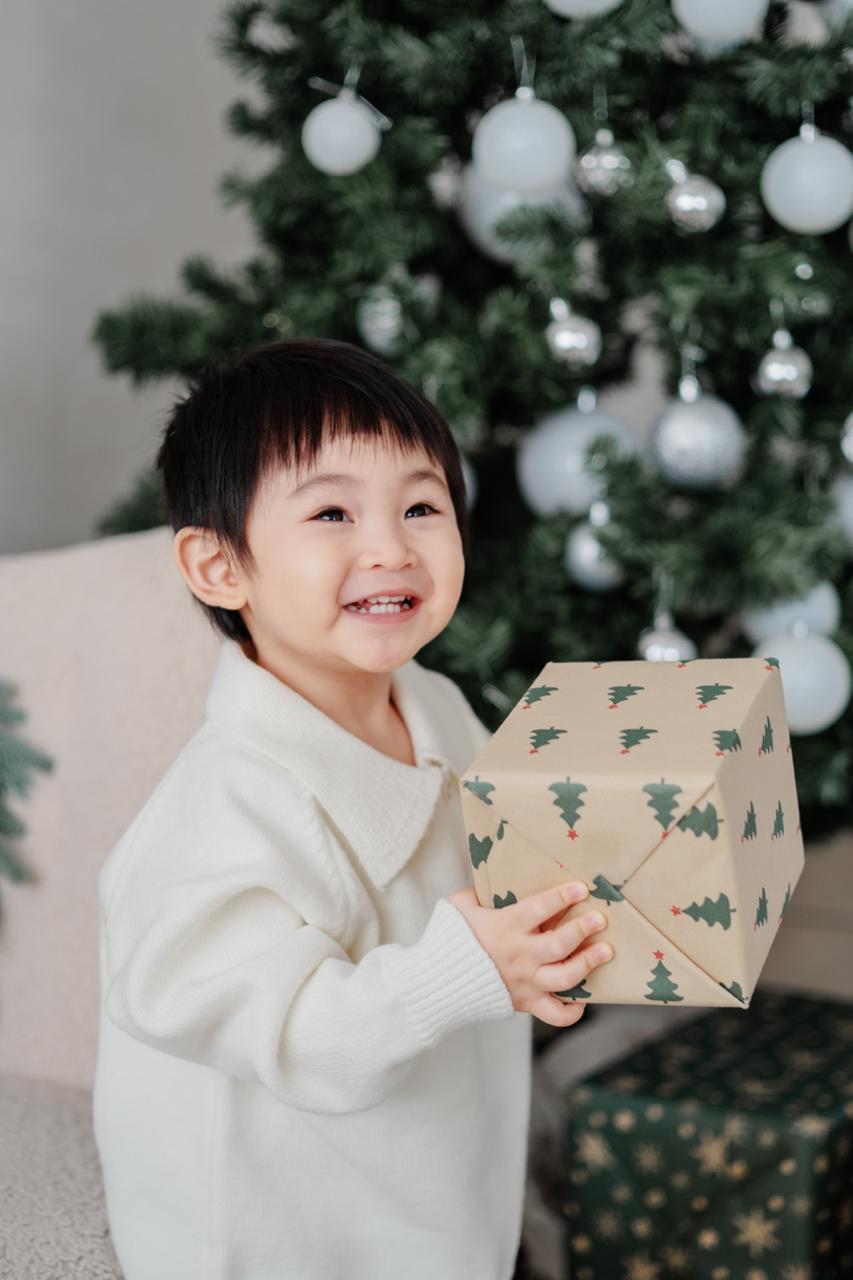 小朋友在聖誕樹旁舉起禮物盒