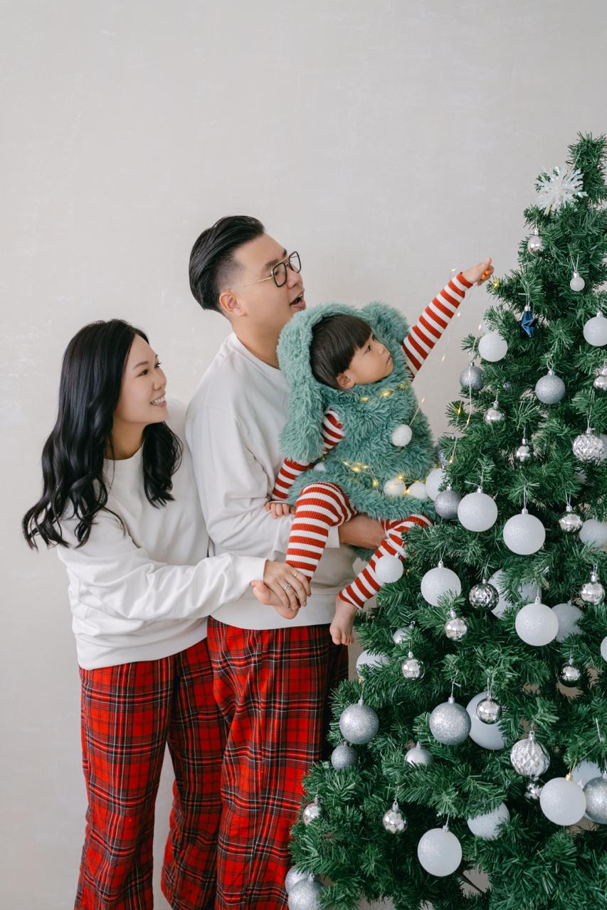 YatYat 一家站在聖誕樹旁，小朋友伸手觸碰樹上的裝飾